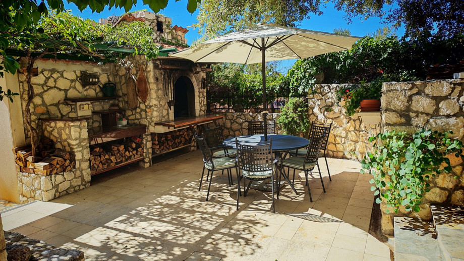 A dedicated charcoal/wood barbecue area is surrounded by stone walls, offering a shaded, traditional spot for outdoor cooking and dining.
