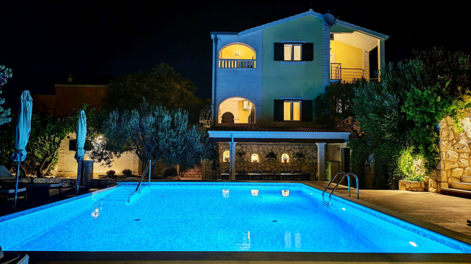 The private swimming pool glows bright blue at night, offering a magical ambience for evening relaxation against the backdrop of the illuminated villa.