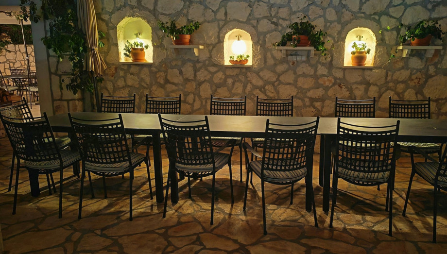 The covered outdoor dining table for 14 is ready for a beautiful evening meal, set against the charming stone wall with softly lit alcoves.