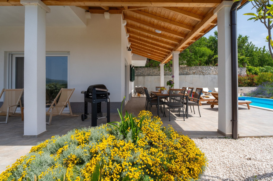 Covered outdoor dining area with a traditional barbecue, and a table for 8 people.