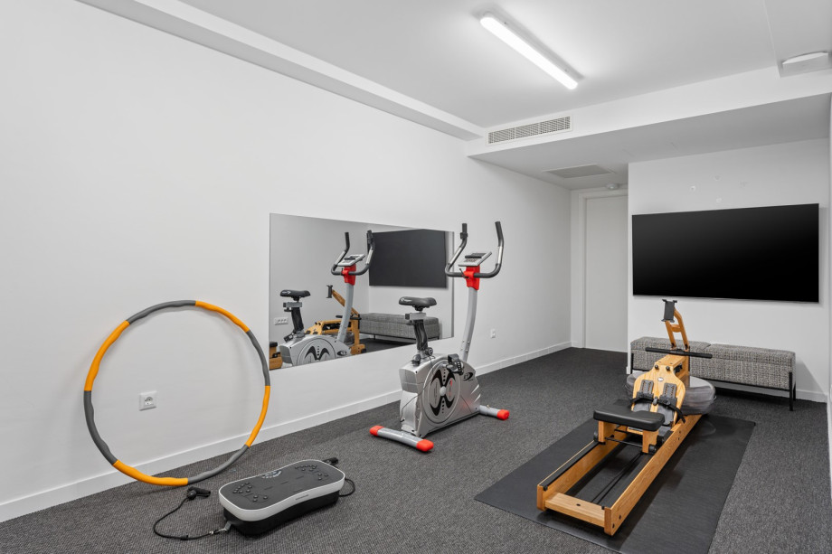 Gym with air conditioning, a TV, an exercise bike, a rowing machine, and a stepper