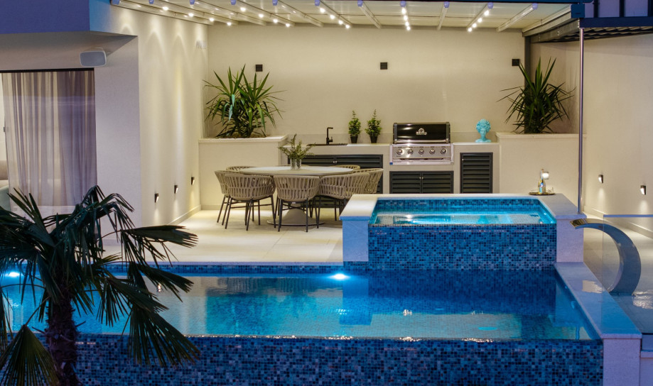 The outdoor area includes a dining spot with a gas barbecue and the beautifully lit pool with its hydromassage area.