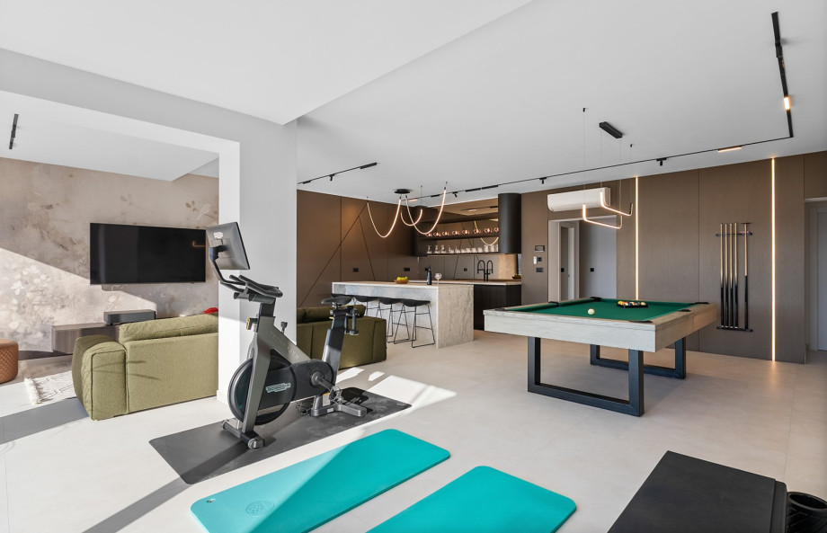 The spa and fun zone, accessible via indoor and outdoor staircases, includes a kitchenette, a billiard table, a cosy sofa, and a well-equipped gym area.
