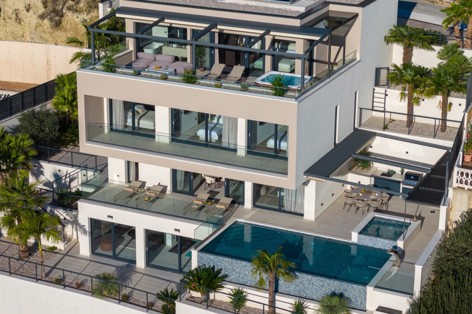 This exterior view shows the private, fenced property over four levels, highlighting the heated infinity pool and the hot tub (whirlpool) terrace.