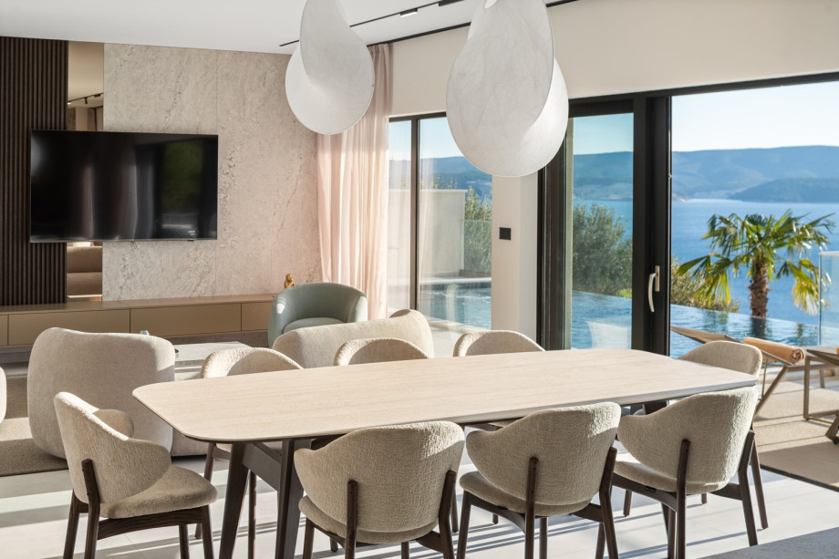 The indoor living and dining area, spanning 65 sqm at pool level, is furnished with comfortable seating and a large dining table.