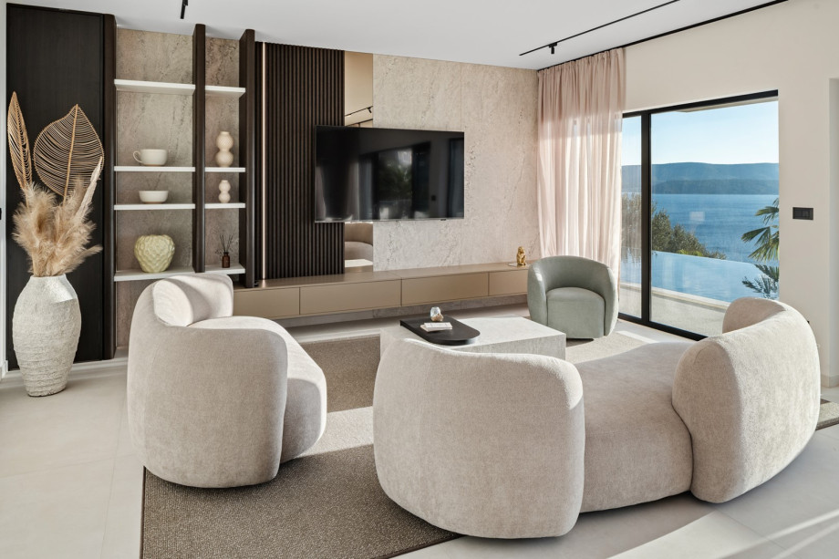 The living room is furnished with comfortable sofas and has large floor-to-ceiling glass sliding doors that open to the pool.