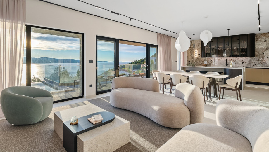The indoor living and dining area is a spacious room furnished with comfortable sofas and a dining table, overlooking the sea.