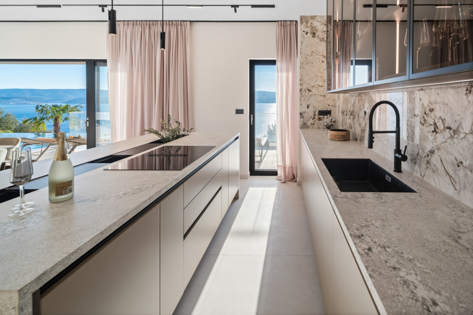 The fully equipped kitchen includes a sleek kitchen island with a cooktop and counter space, offering views out toward the sea.