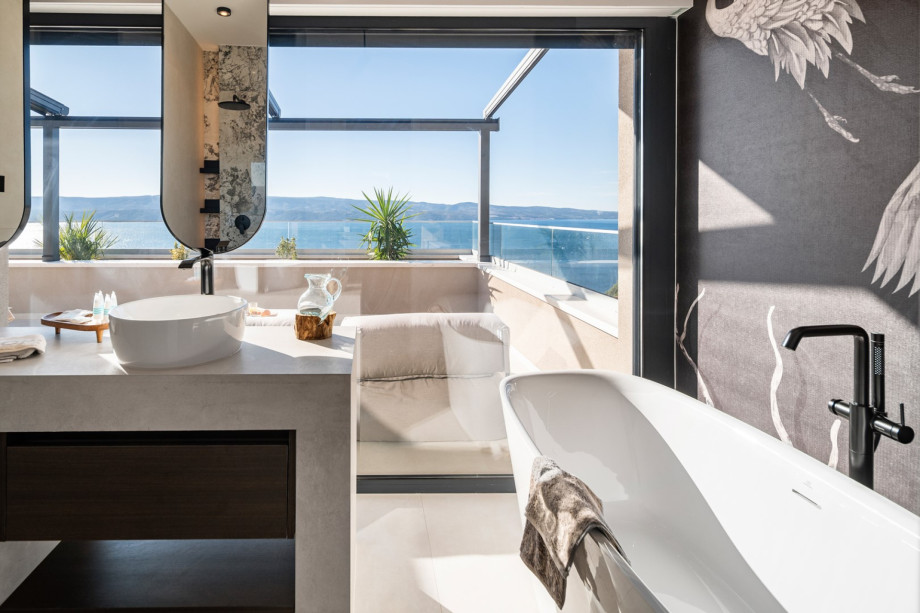 The en-suite bathroom of the master bedroom features a freestanding bathtub, double sinks, and views over the terrace and the sea.