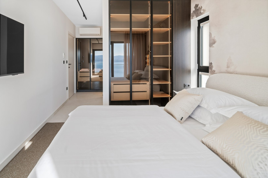 This stylish bedroom includes a wall-mounted TV and a large, glass-fronted wardrobe.