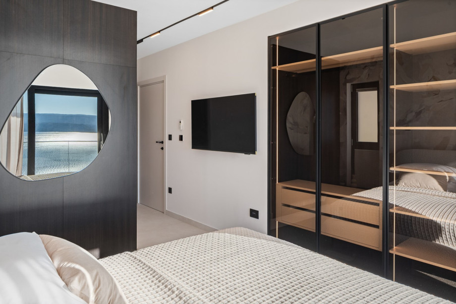 This bedroom is exceptionally organised, featuring a comfortable bed, a glass-fronted wardrobe, and is equipped with all modern amenities for a very comfortable stay.