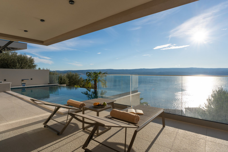 This image captures the sun deck surrounding the private, heated infinity pool with deck chairs and sea views.