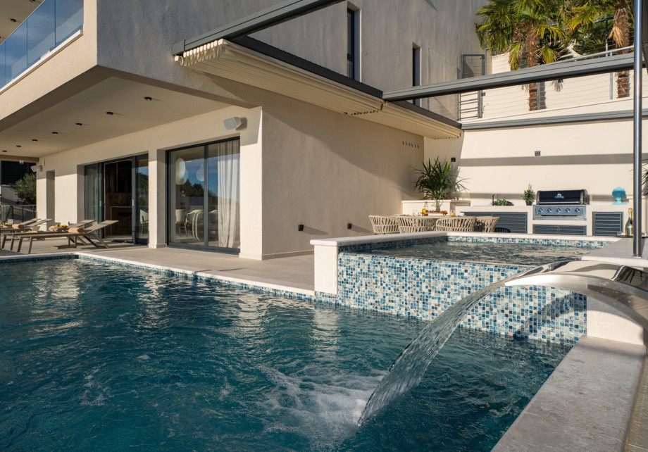 The private, heated infinity pool, measuring 8m x 4m, is shown with its waterfall feature and attached hydromassage area.