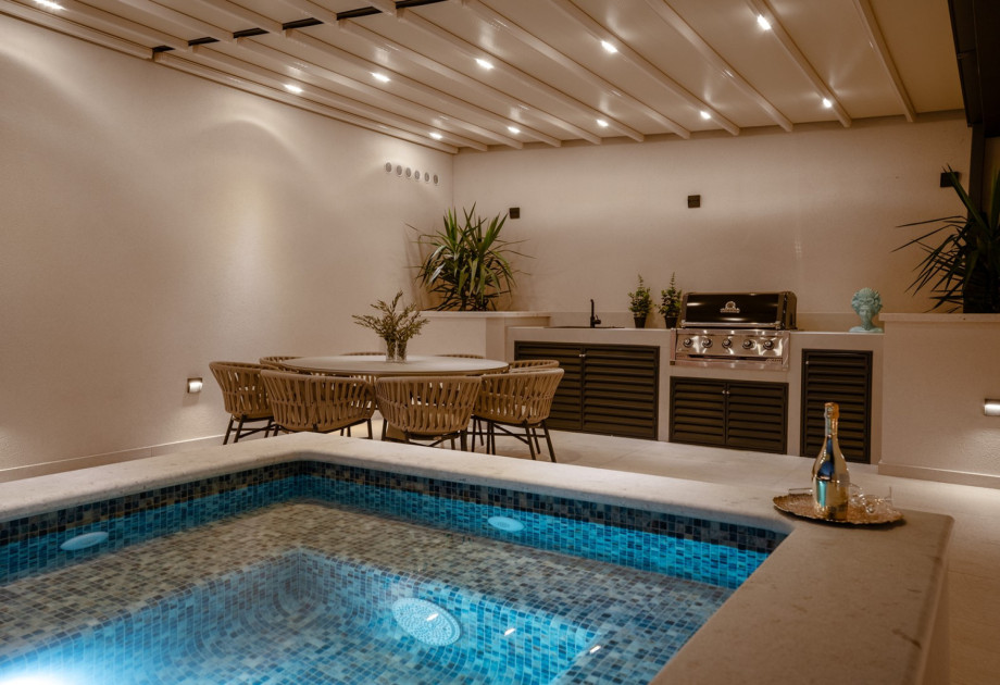 The outdoor dining area with a gas barbecue and a view of the attached hydromassage area of the pool.