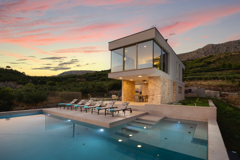 The exclusive villa features a heated pool and stunning design against a backdrop of mountains at sunset.