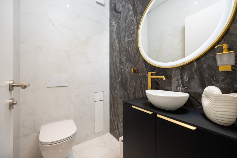 An elegant toilet boasts luxurious marble walls, modern fixtures, and a stylish gold-rimmed mirror.