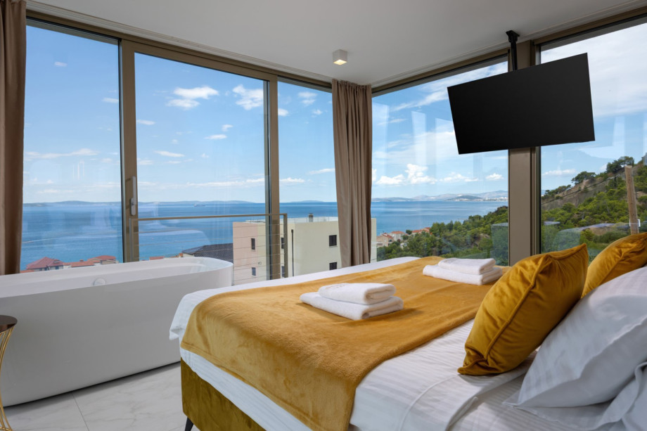King-size bed and bathtub in Bedroom 1, offering magnificent sea and pool views through the glass wall.