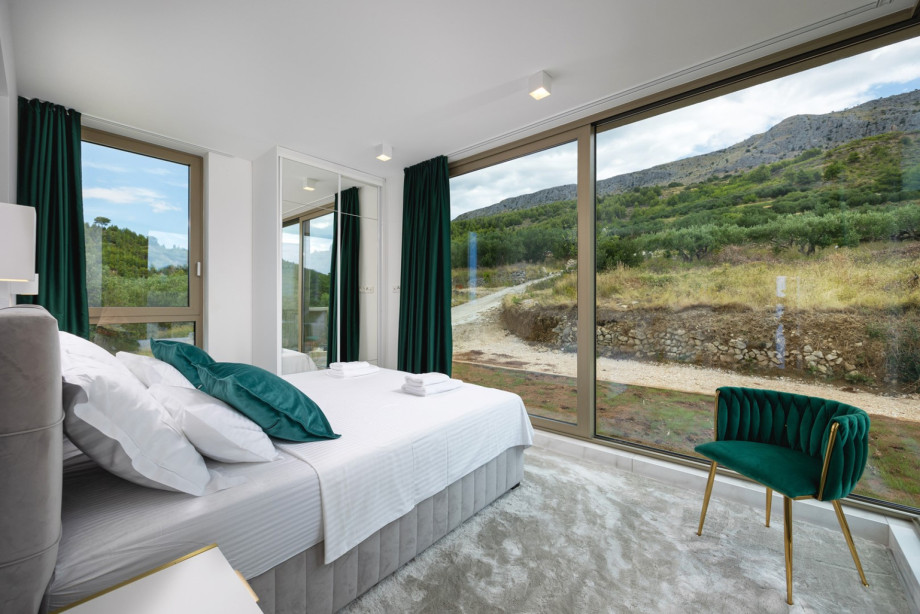 Bedroom 4 (16 sqm) with a King-size bed and en-suite bathroom, offering views of olive groves and mountains.