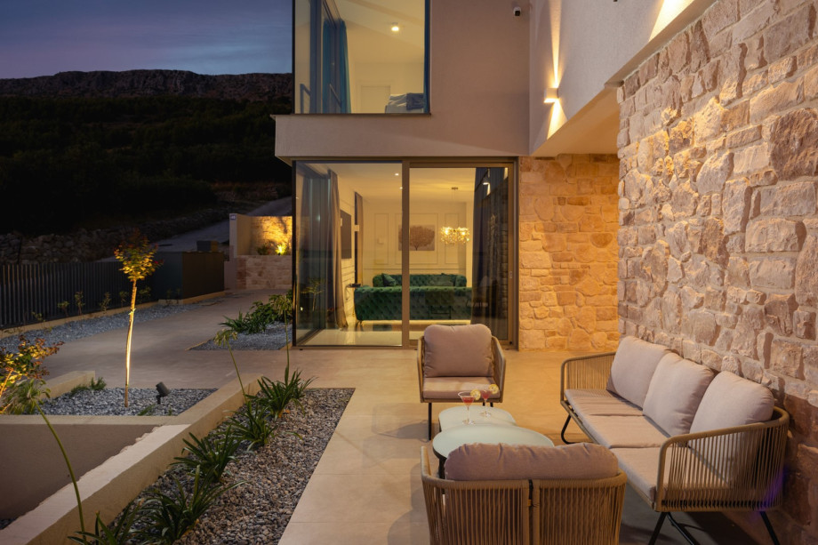 The covered outdoor lounge area at dusk, featuring stone columns and connecting to the living room via sliding doors.