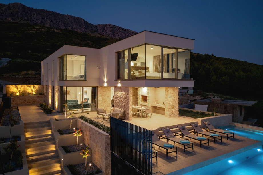 The two-level villa, sprawling over 203 sqm, is illuminated at night, highlighting the pool and outdoor dining area.