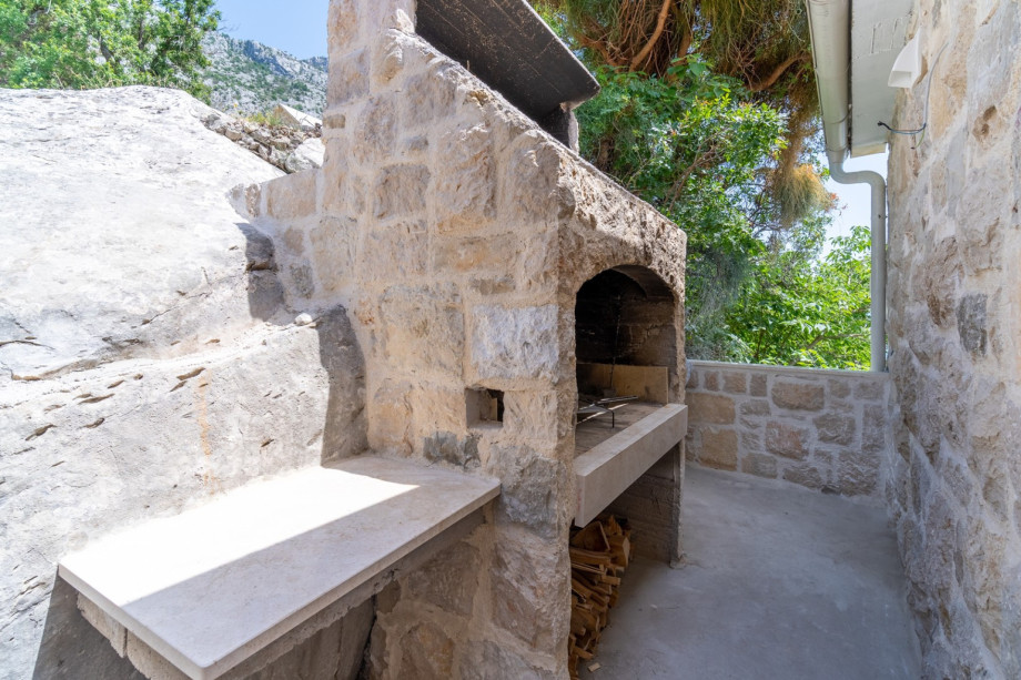 A traditional barbecue is located next to the main entrance to the house, next to the outdoor dining area.