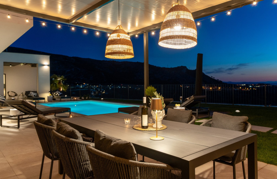 Covered al fresco dining area lit at night, featuring a large table and views of the inviting pool.