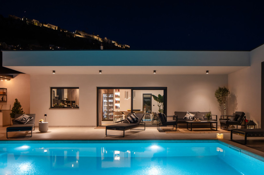 Night view of the pool and lounge area, with glass doors opening to the stylish interiors.
