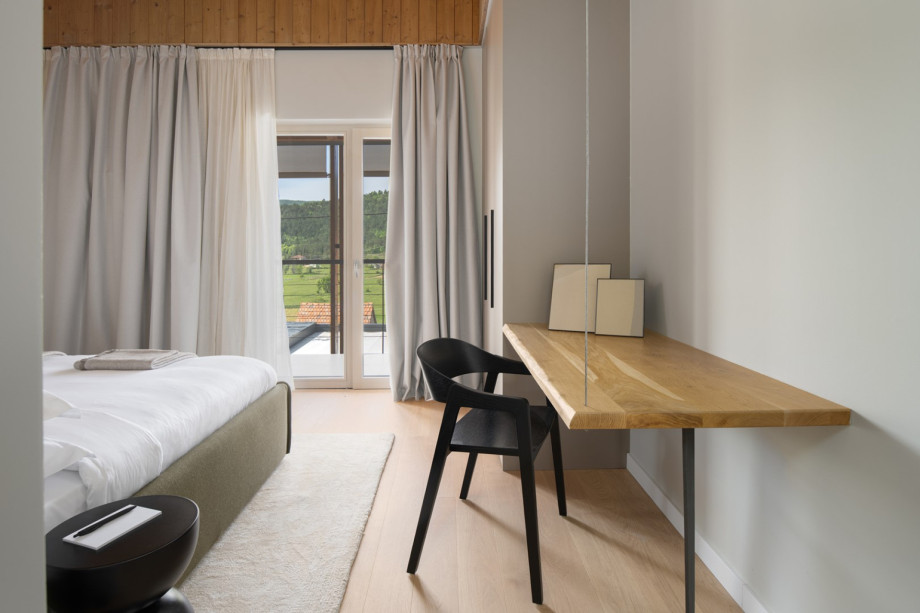 This bedroom features a wooden desk, a chair, and large windows with countryside views.