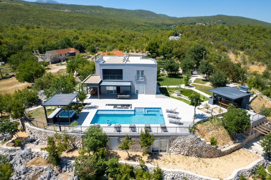 View of the villa, stone-walled terraces, and landscaped grounds set in a quiet rural landscape.