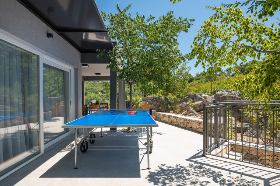 Shaded terrace with a table tennis setup, perfect for games next to the garden and rock walls.