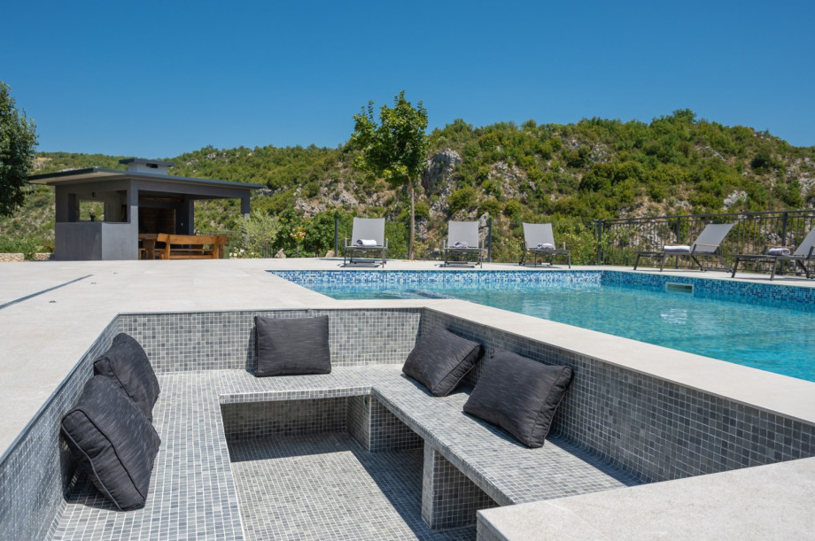 A sunken lounge area with mosaic tiles and cushions is built into the pool deck.