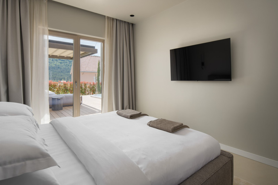A modern bedroom equipped with a flat-screen TV and glass doors leading out to a private wooden deck.