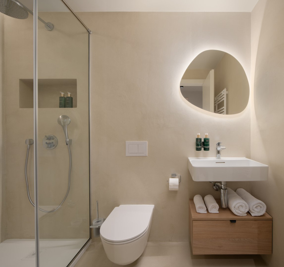 A modern bathroom with a shower, sleek toilet, and a backlit mirror on the wall.
