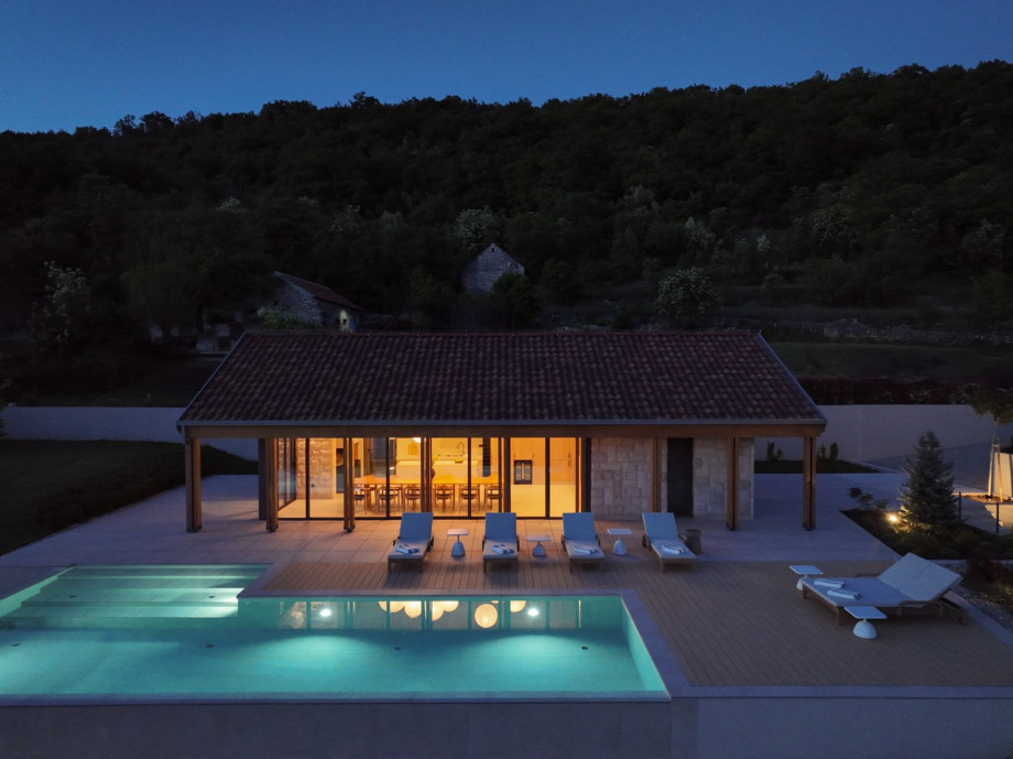 Evening view of the illuminated private pool and sunbathing area, perfect for relaxing.
