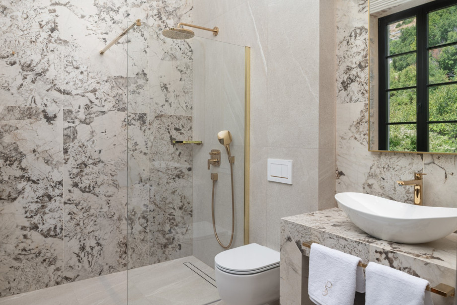 An elegant en-suite bathroom features a walk-in shower with premium gold fixtures and stone finishes.