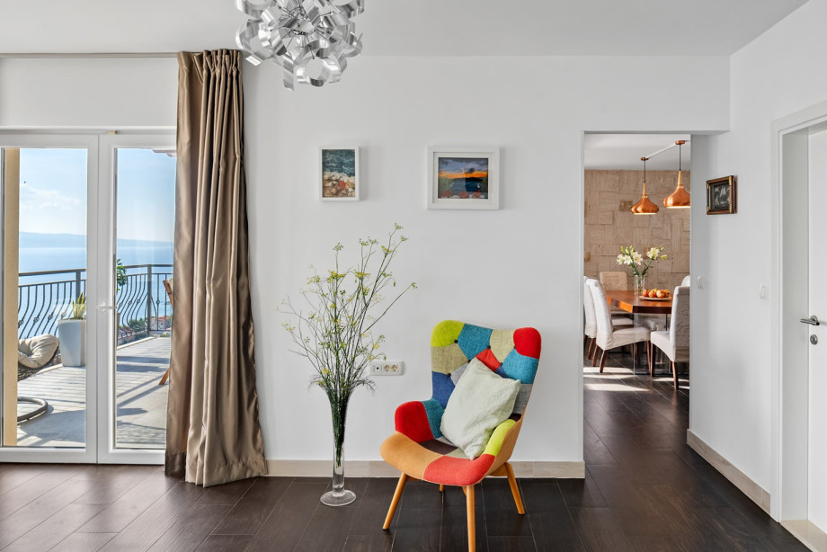 A colorful patchwork armchair provides a vibrant focal point in the hallway, leading towards the dining area and the balcony with sea views