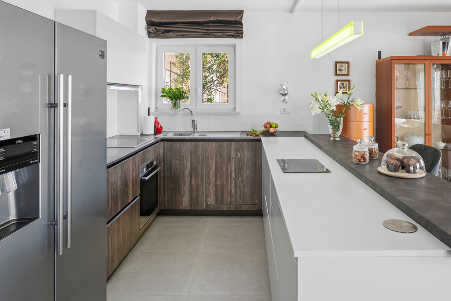 A fully equipped kitchen boasts sleek, wooden cabinetry, integrated appliances, and a central white counter perfect for additional prep space