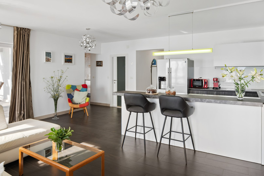 The main kitchen and bar area, with high black stools and bright white cabinets, opens directly into the main living room, creating a seamless social space