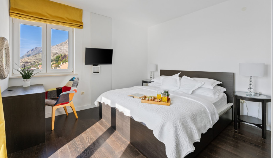 A brightly lit master bedroom features a king-size bed, a wall-mounted TV, and A/C