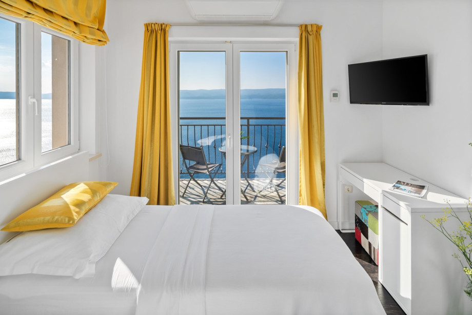 Bedroom No. 3 features a stunning sea view and balcony access, decorated with cheerful yellow curtains and includes an integrated workspace