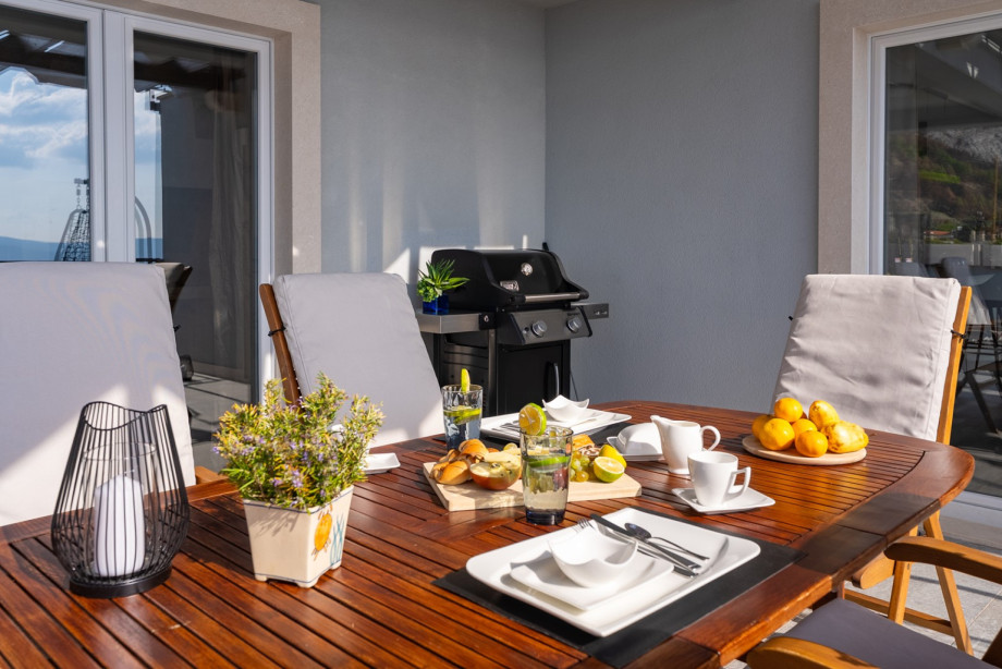 The outdoor dining table is perfectly set for a meal, complete with a modern BBQ grill nearby for easy outdoor cooking