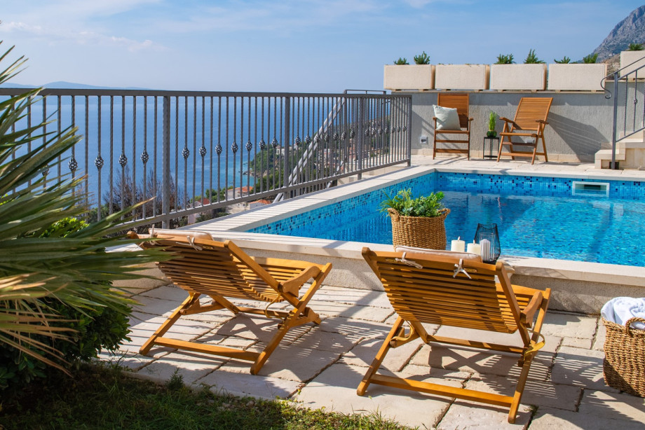 A spacious sun deck features wooden sun loungers by the pool, enhancing the comfortable setting