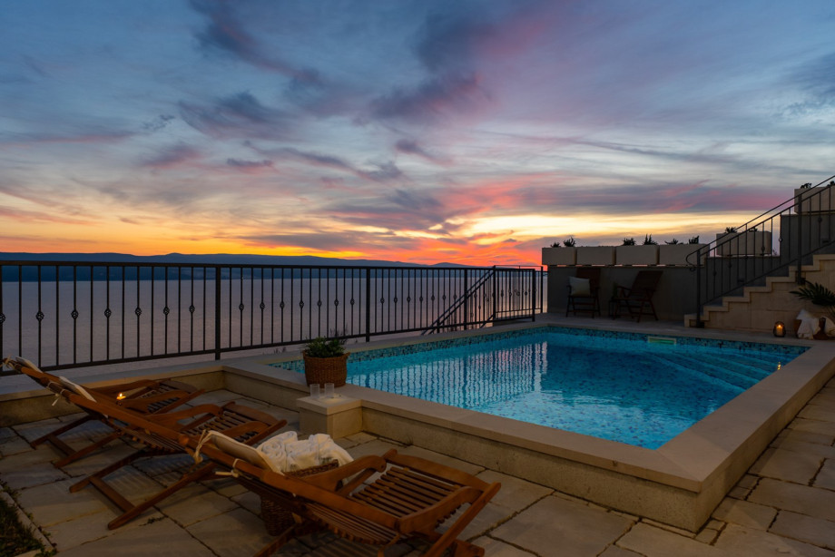 The pool area at dusk is illuminated by the beautiful glow of a red-and-orange sunset over the Adriatic horizon
