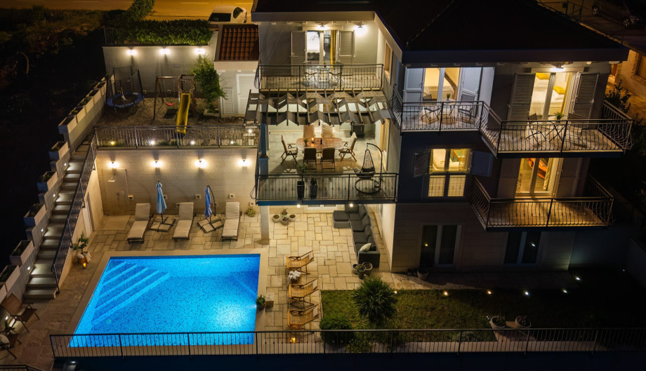 A stunning night-time aerial view showcases the full layout of the luxurious villa, illuminated outdoor areas, and private pool