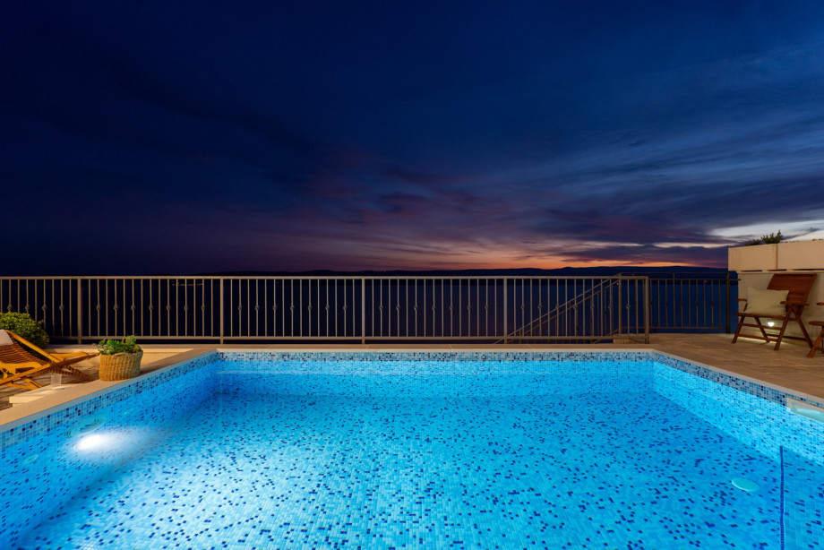 The serene, illuminated pool reflects the deep blues and subtle orange hues of the sky just after the sun has set over