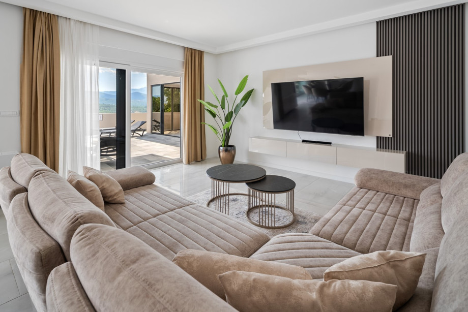 Comfortable sofas are arranged around a flat-screen TV, while large glass doors lead directly to the pool area, blending indoor and outdoor living seamlessly
