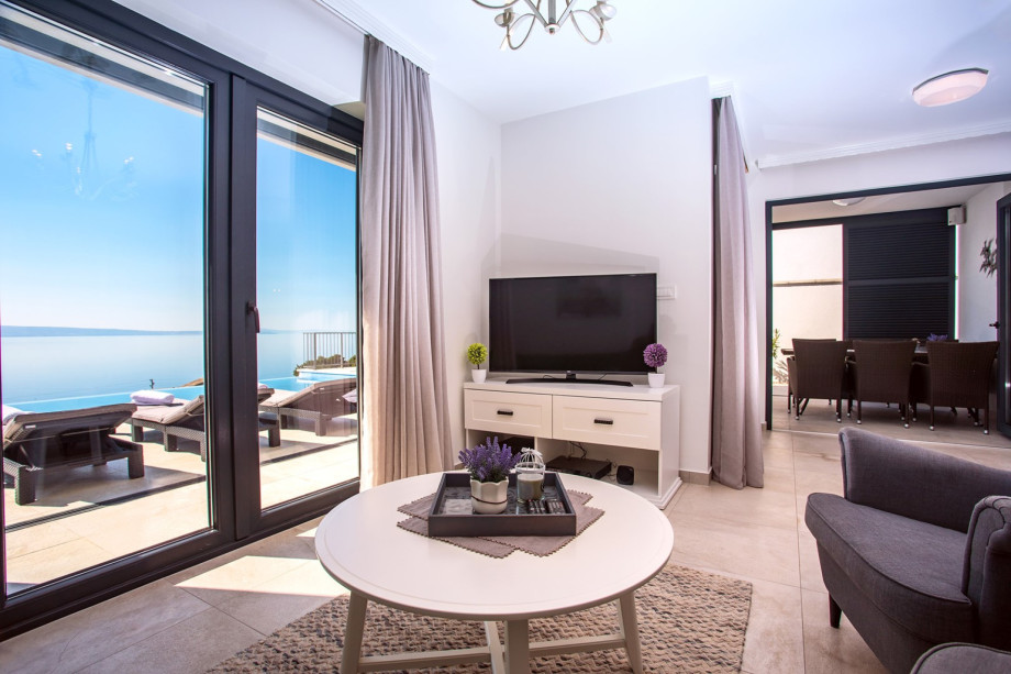 Living area with glass walls toward pool and outdoor dining area with sea views