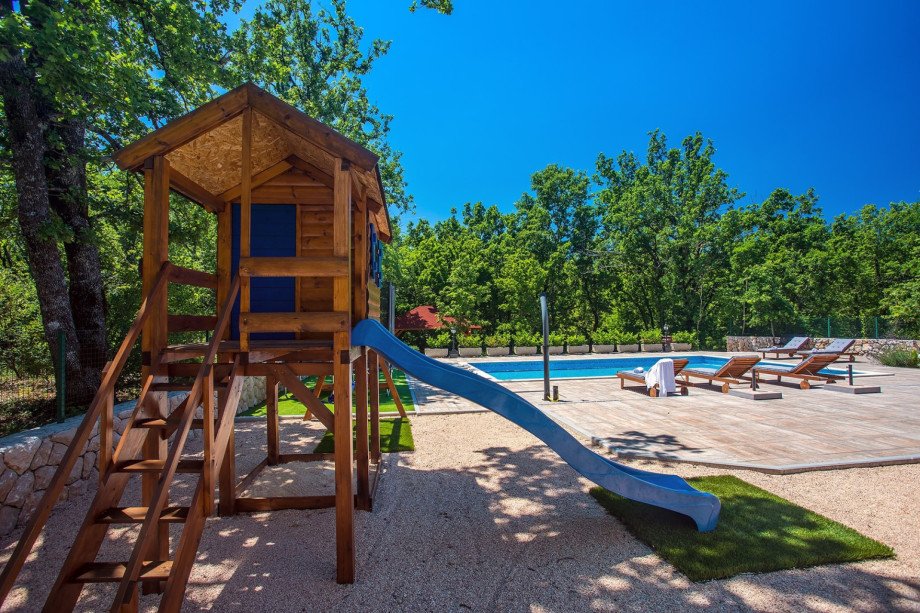 A place for the kids with trampoline, swing and a wooden playhouse with a slide