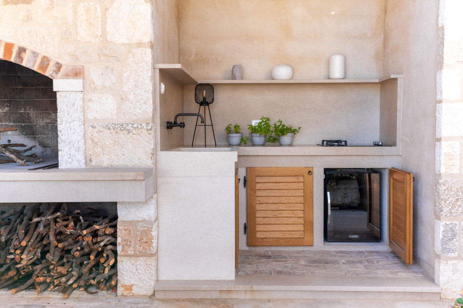 A summer kitchen with a stove, a wine cooler, and a traditional barbecue.