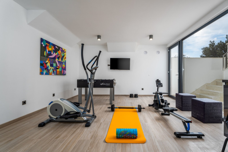 Basement area equipped with a TV, Table soccer, Rowing Machine, Exercise bike, Weights, and a Pilates ball.